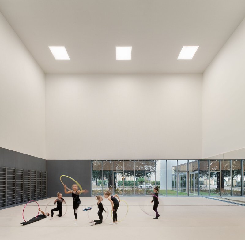 Rhythmic gymnastics studio with children practicing under three square skylights and glazed courtyard view