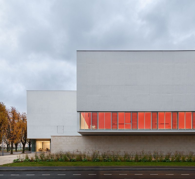 Street view of the corrugated metal facade with red louvered panels and autumn trees in the background