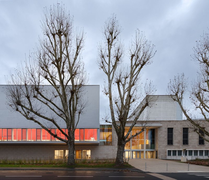 Main entrance with bare winter trees framing the limestone base and red louvered upper level