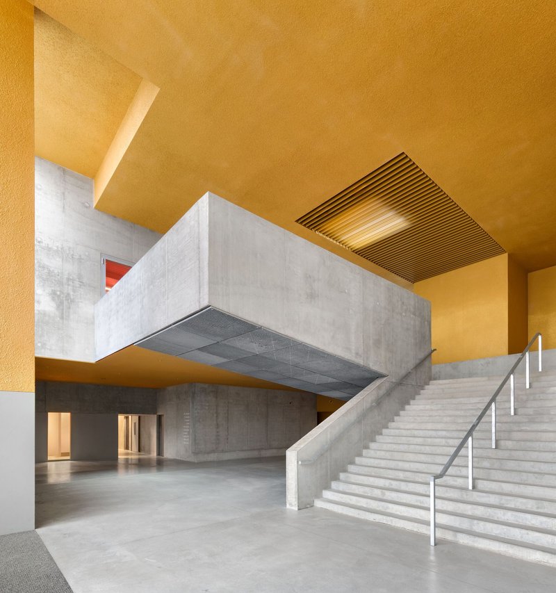 Interior foyer with concrete staircase and suspended volume beneath a golden ochre ceiling