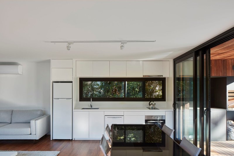 Open plan kitchen with white cabinetry, horizontal window and folding glass doors to timber deck