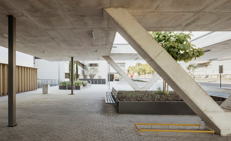 Covered porch with diagonal concrete columns, planted beds, benches, and board-formed concrete ceiling