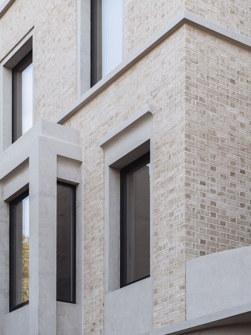 Detail of pale brick and white render meeting at the facade corner with recessed window openings