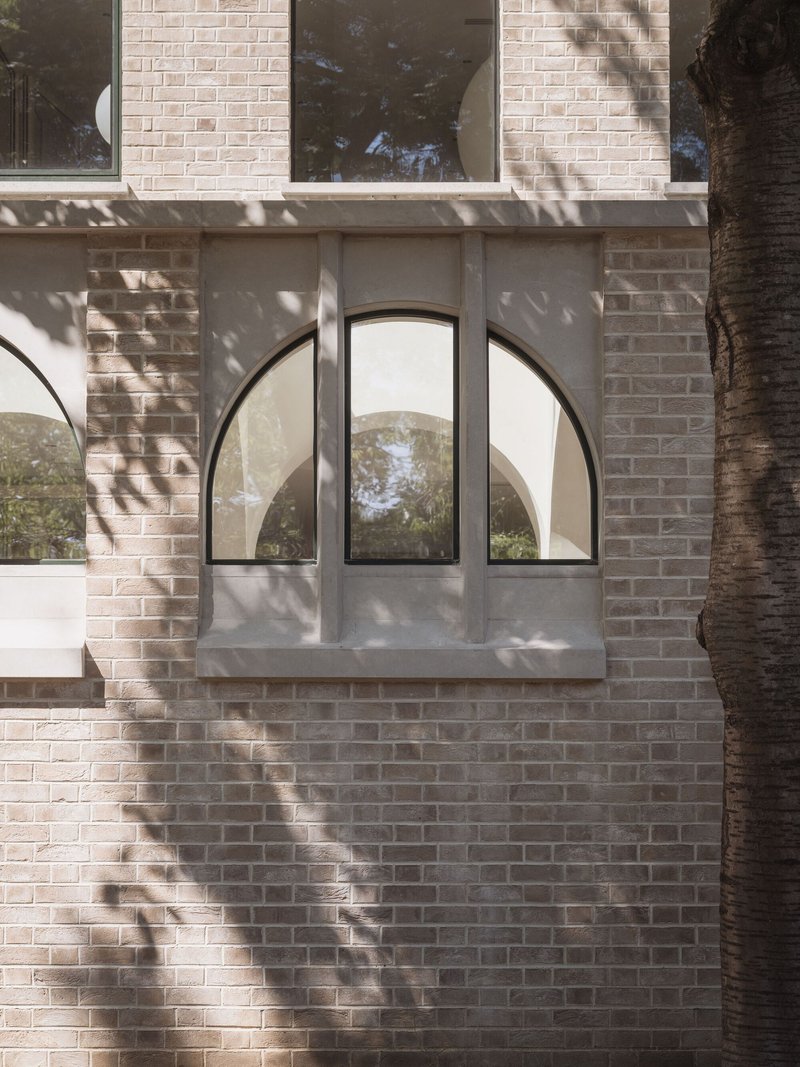 Arched window with steel frames set in pale brick with dappled tree shadows across the wall