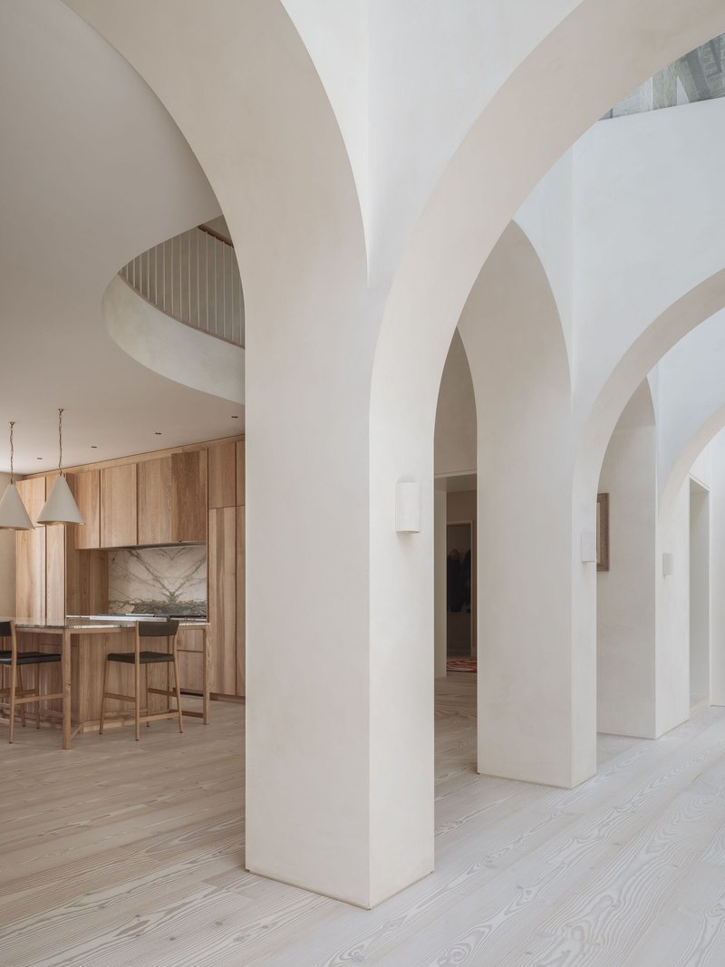 Interior view through white arched openings toward the timber kitchen across pale oak flooring