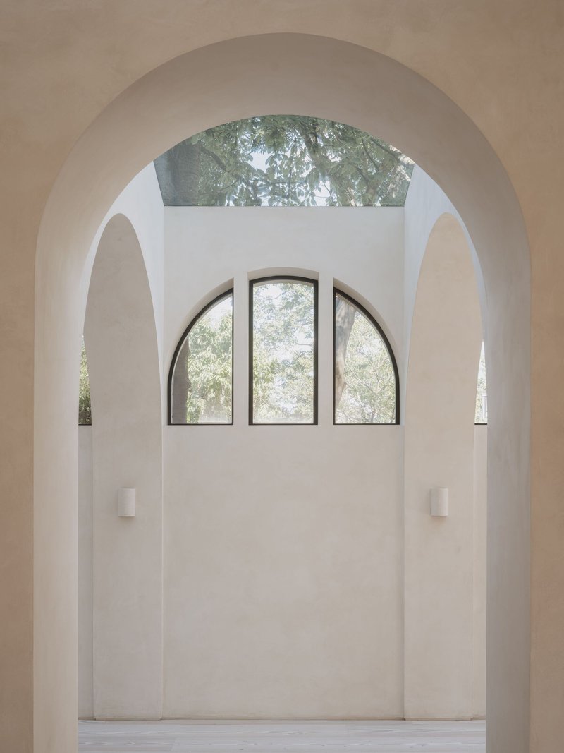 Arched window framed within layered vaulted openings and a skylight above filtering green foliage