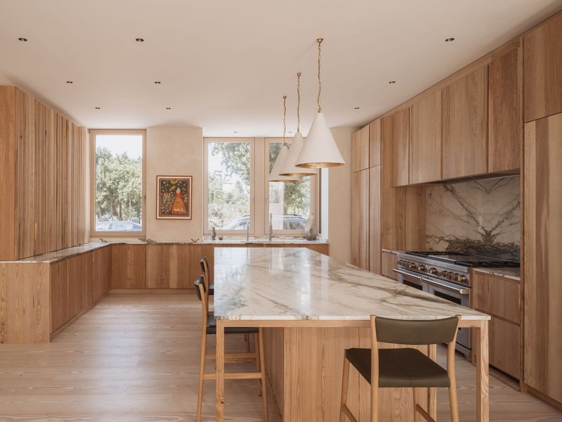 Kitchen with oak cabinetry and central island clad in veined marble under white pendant lights