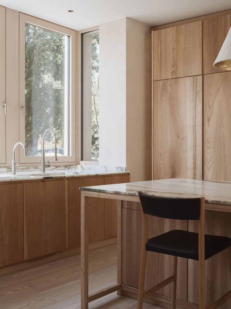 Corner sink with marble countertop beneath a tall window framing leafy trees outside