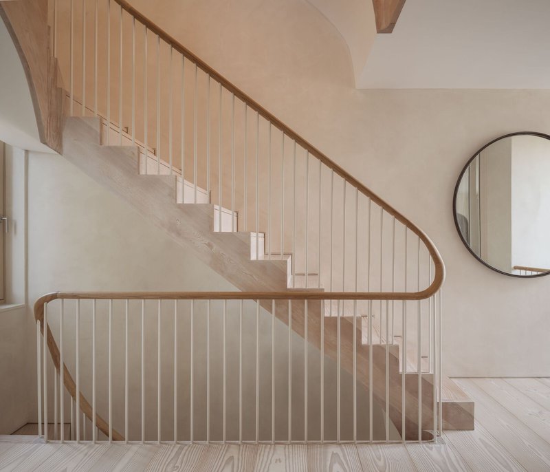 Timber staircase with curved handrail and vertical balusters beneath a vaulted plaster ceiling