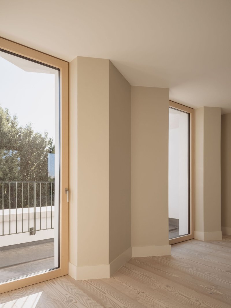 Interior corner with pale timber-framed glazed doors opening to a balcony and adjacent room with olive tree visible outside