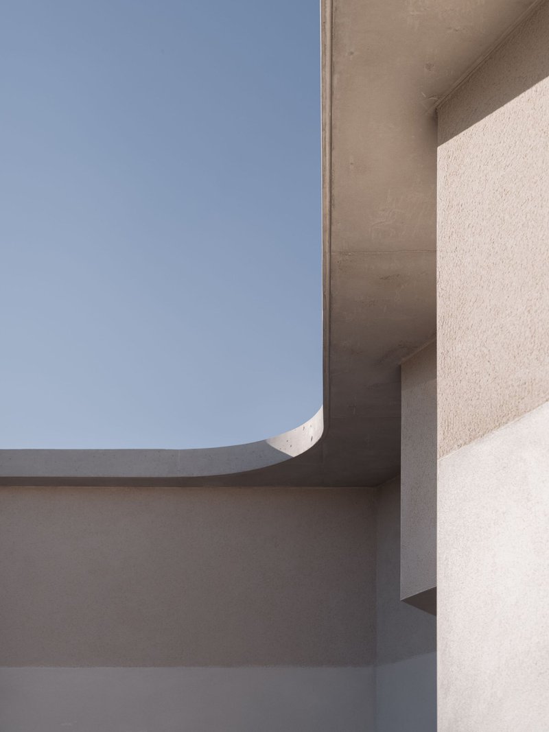 Close-up of curved plaster ceiling soffit meeting textured white wall under clear blue sky