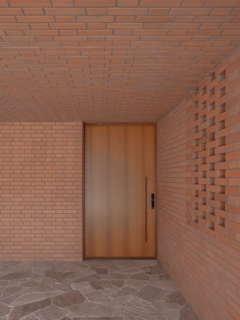 Entry vestibule with timber door flanked by flat and textured brick walls under brick ceiling