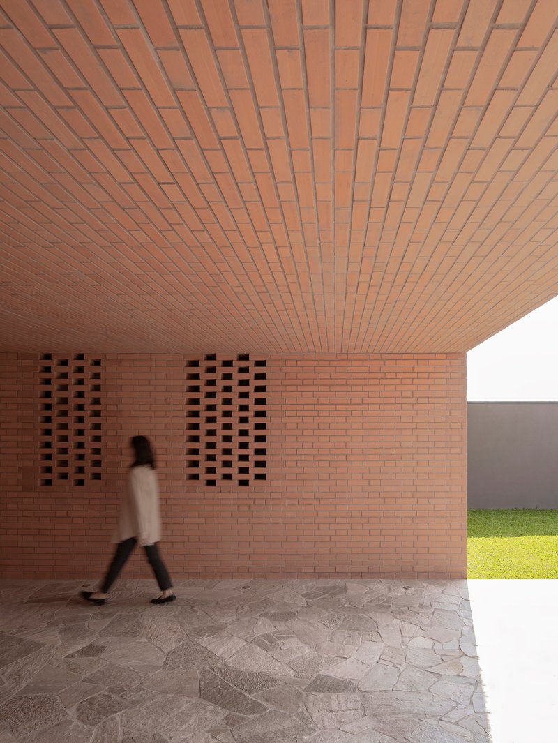 Covered entry passage with brick ceiling and perforated wall panels as a figure walks through