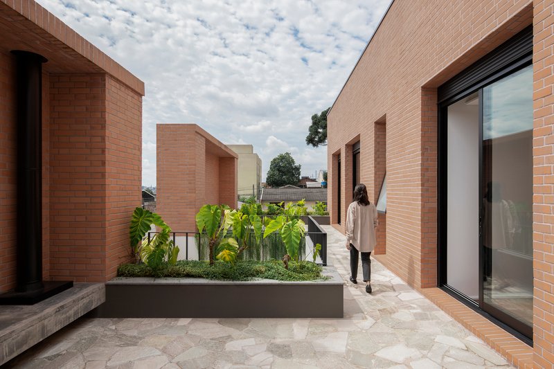 Rooftop terrace with raised planting beds and brick volumes framing views under a cloudy sky