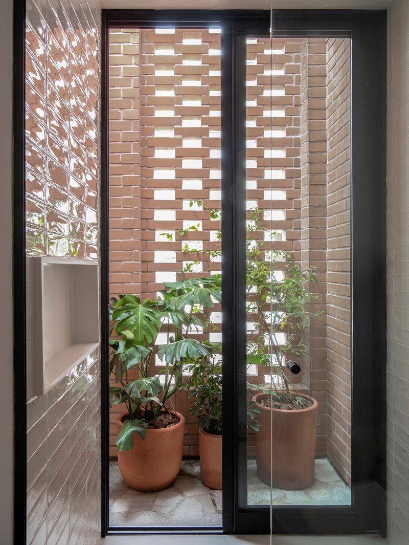 Interior view through glass door to narrow courtyard with perforated brick screen and potted plants