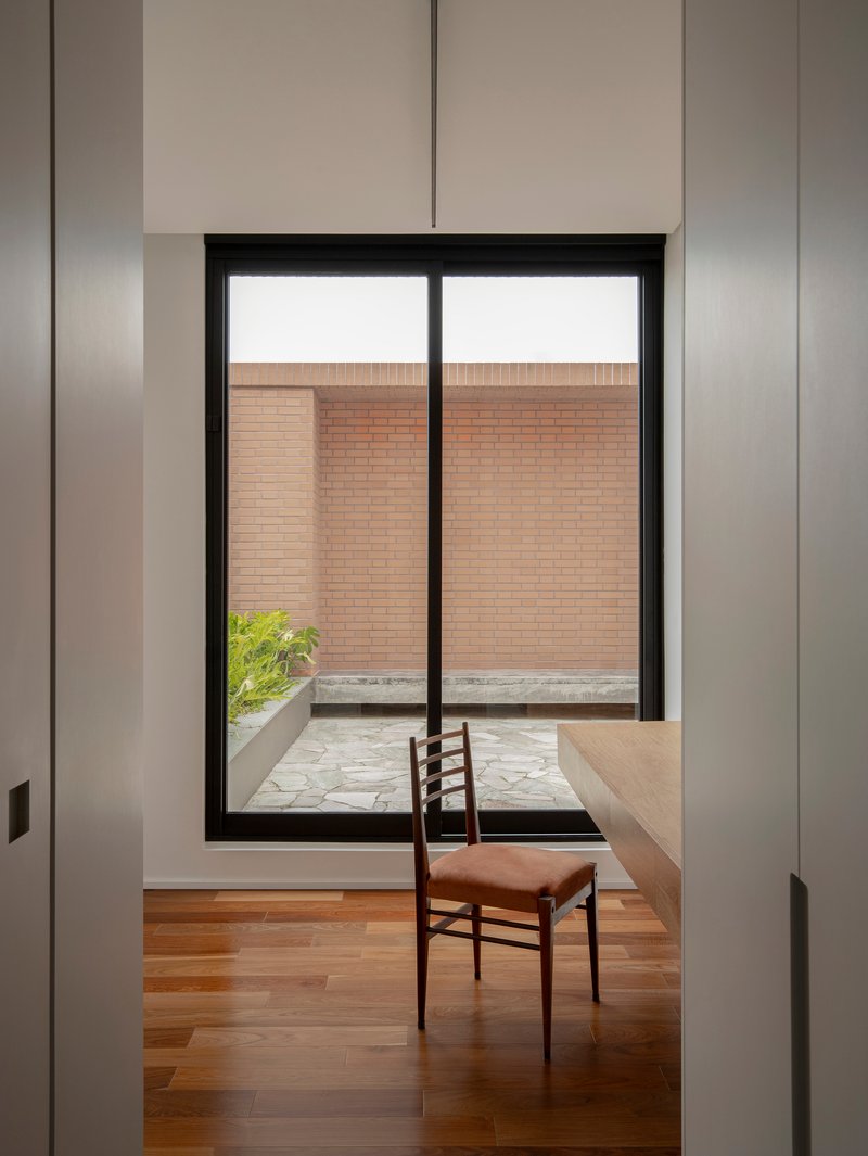 Interior workspace with timber desk and single chair framed by white walls and black window