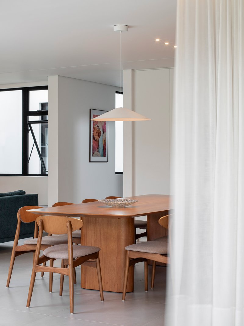 Dining area with timber table and pendant light viewed through a white curtain