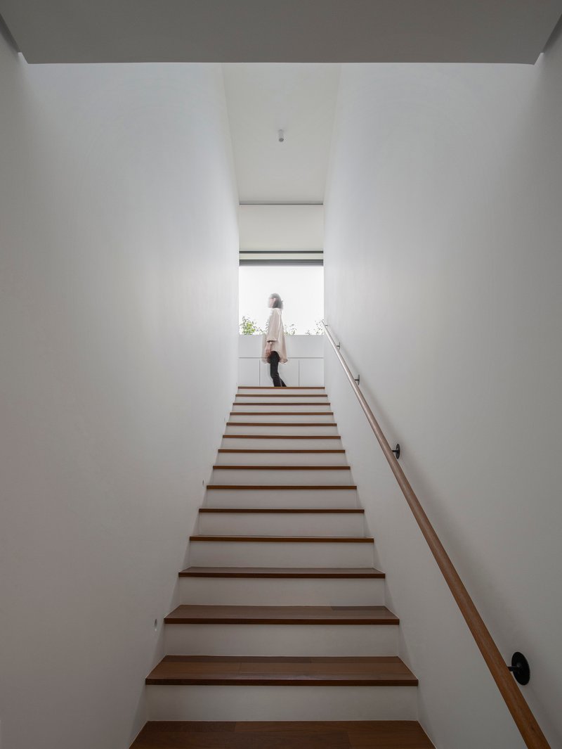 Timber staircase rising between white walls with a figure at the top landing