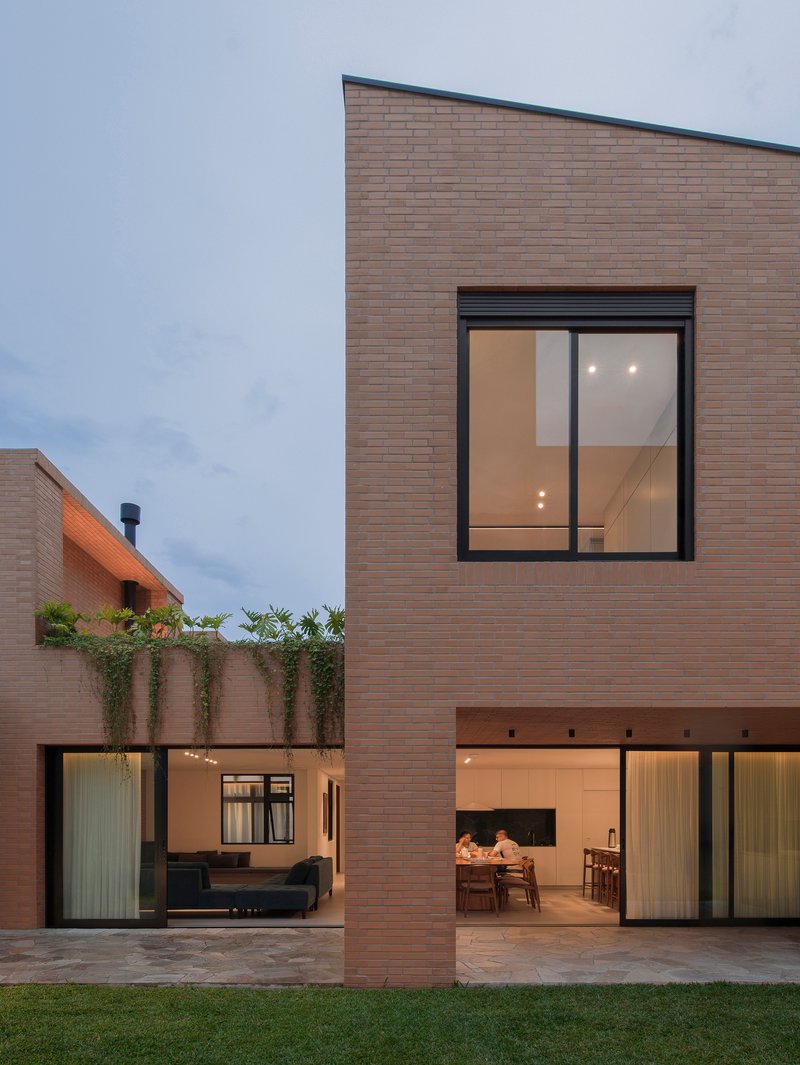 Two-story brick residence with glazed openings and courtyard at dusk