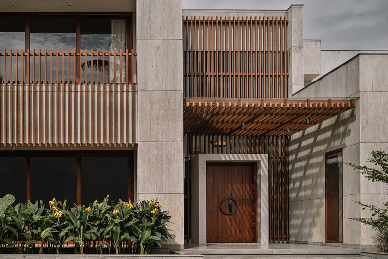 Facade detail with vertical timber screens, concrete frame, and planted bed casting shadows