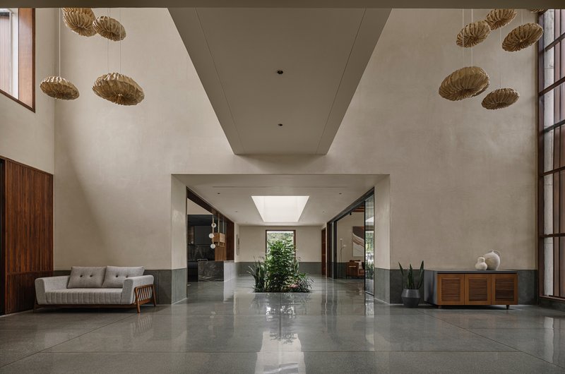 Double-height entry hall with polished grey floor, woven pendant lights, and planted interior courtyard beyond