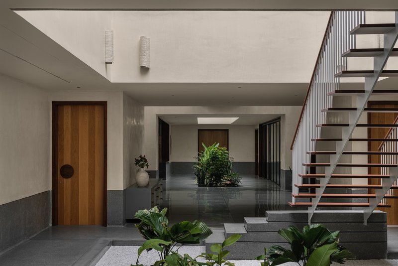 Interior courtyard with open-tread timber staircase, skylight, and planted beds between polished stone pavers