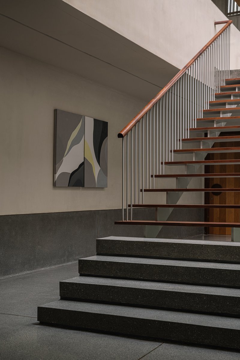 Detail of timber-tread staircase with vertical metal balusters and timber handrail against two-tone wall