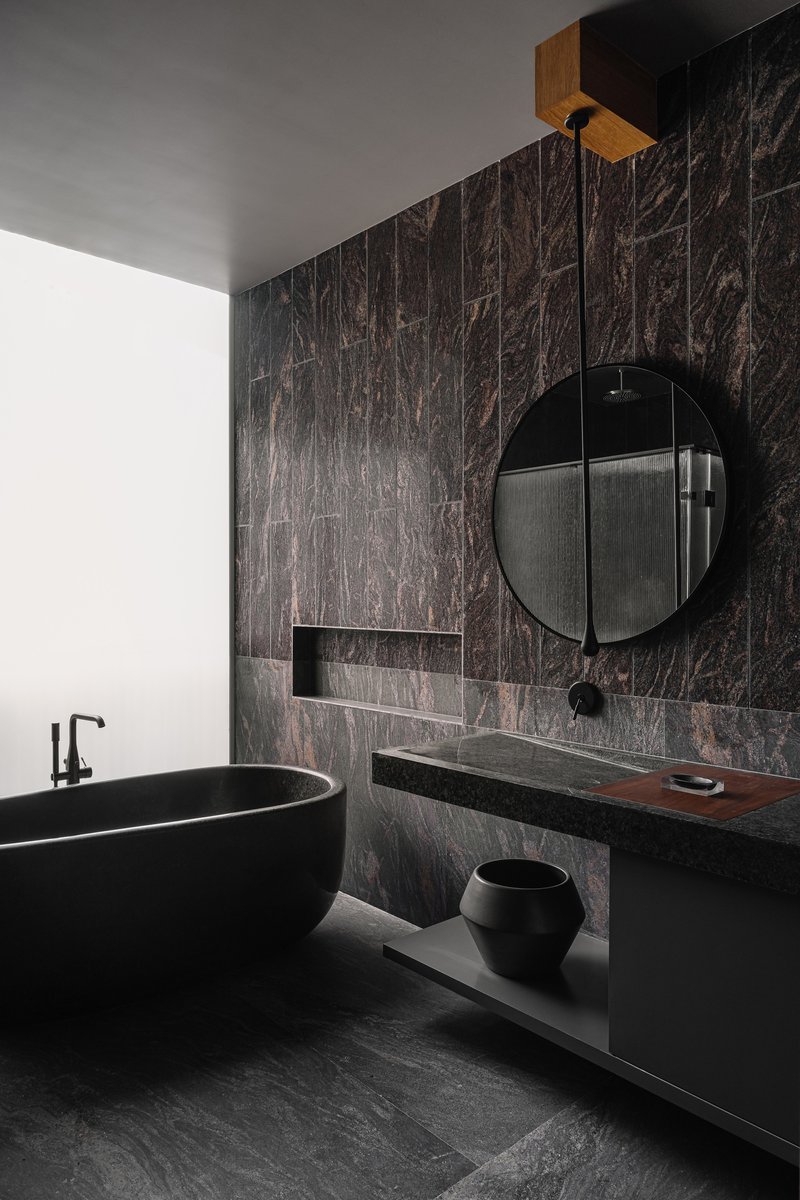 Bathroom with dark marble wall tiles, black freestanding tub and floating vanity with round mirror