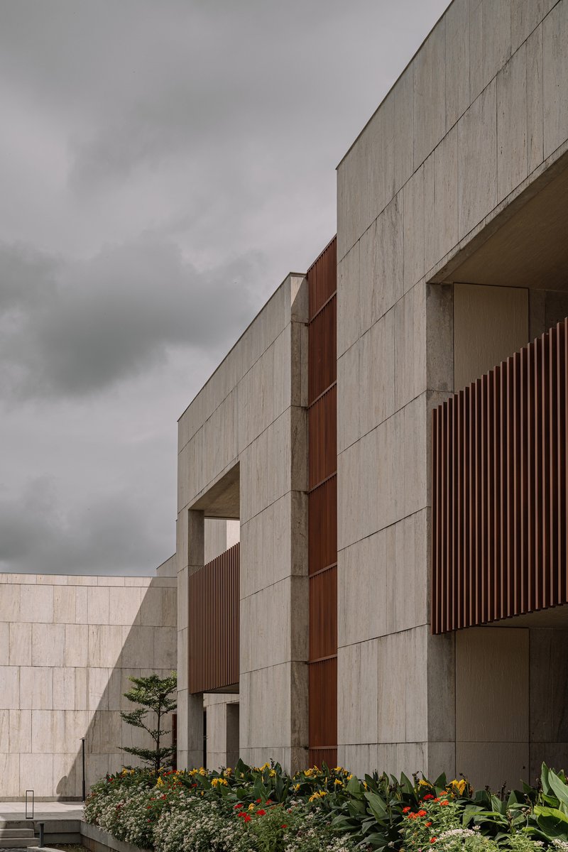 Concrete panel facade with vertical timber screens and planted bed under an overcast sky