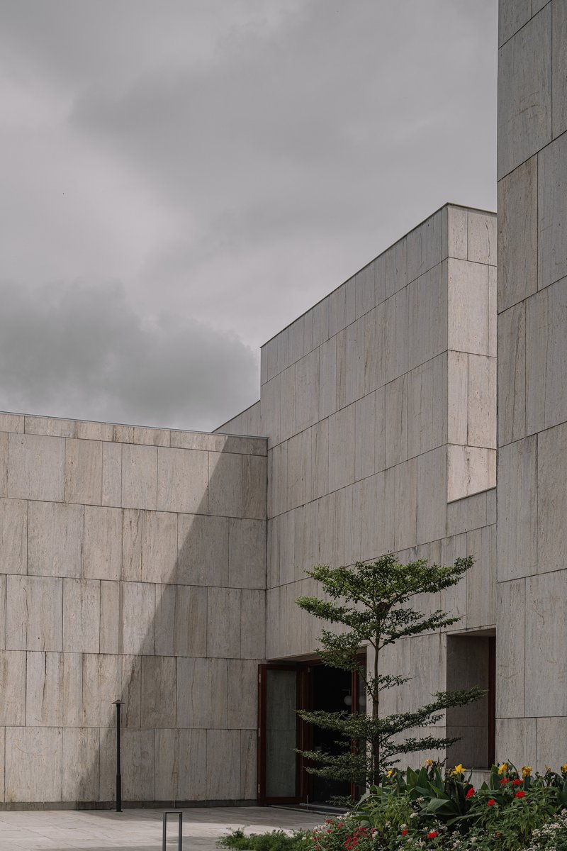 Courtyard view of interlocking concrete walls with a sculpted pine tree beside a recessed entrance