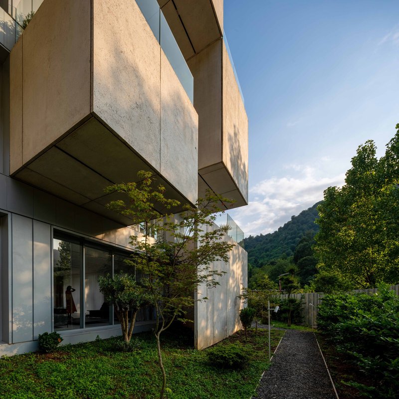 Side view of stacked concrete volumes with trees between levels and hillside in the background