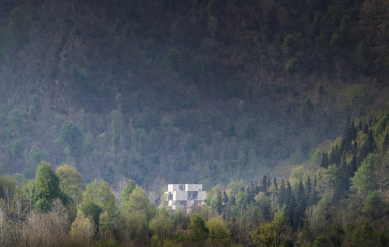 White geometric volumes nestled among deciduous and evergreen forest in morning mist