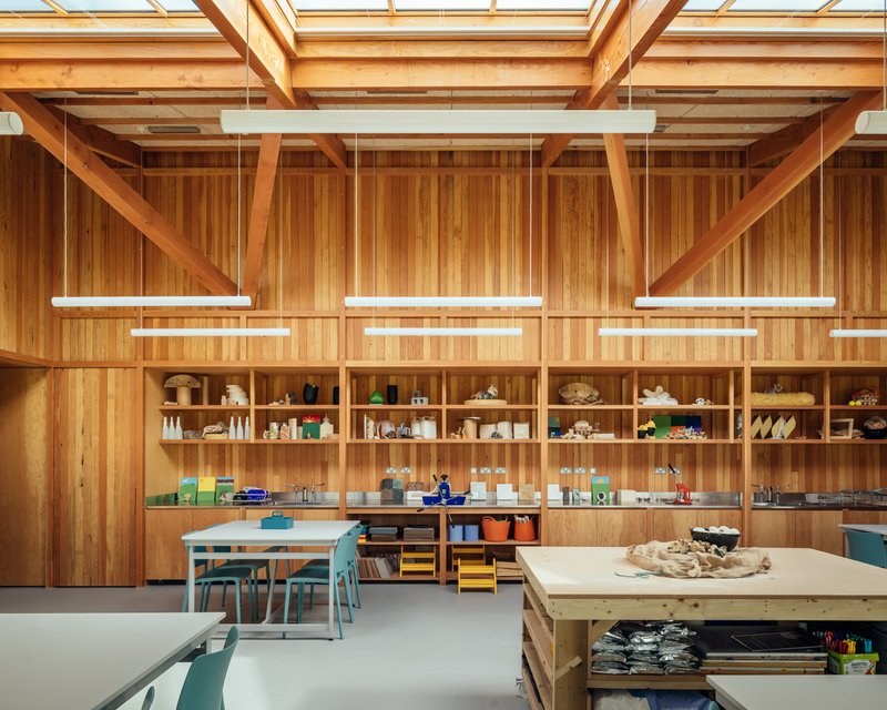 Vertical timber wall with built-in shelving displaying student work beneath suspended linear lighting fixtures