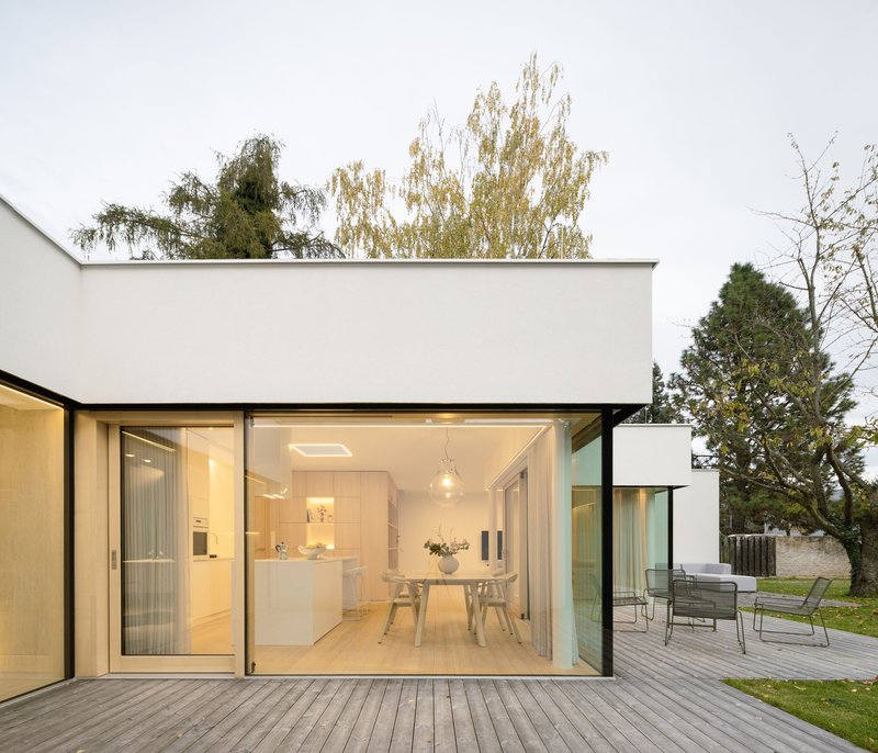 Open sliding glass doors revealing dining area and kitchen from timber deck at dusk