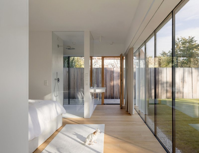 Bedroom with glazed walls opening to courtyard and glass-enclosed shower in morning sunlight