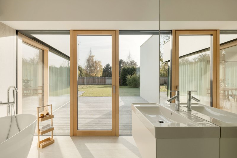 Bathroom with freestanding tub and timber-framed pivot door opening to timber deck and lawn
