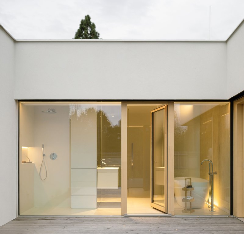 Courtyard view of sliding glass doors opening to a bathroom with timber deck flooring at dusk