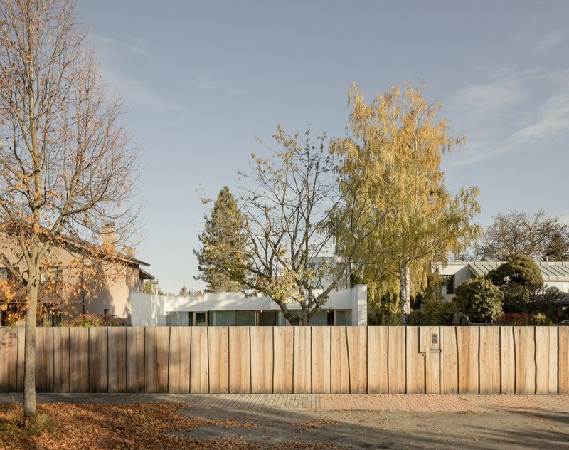 Street view of vertical timber fence screening the residence behind bare and golden autumn trees