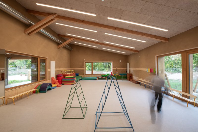 Playroom interior with hempcrete ceiling panels, linear light fixtures and colorful climbing frames with moving figure