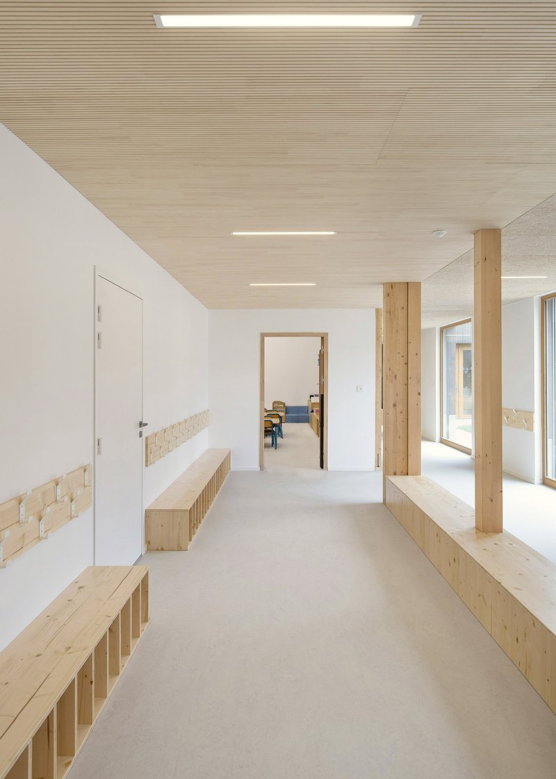 Corridor with timber columns, built-in benches, and wood-paneled ceiling under recessed linear lighting