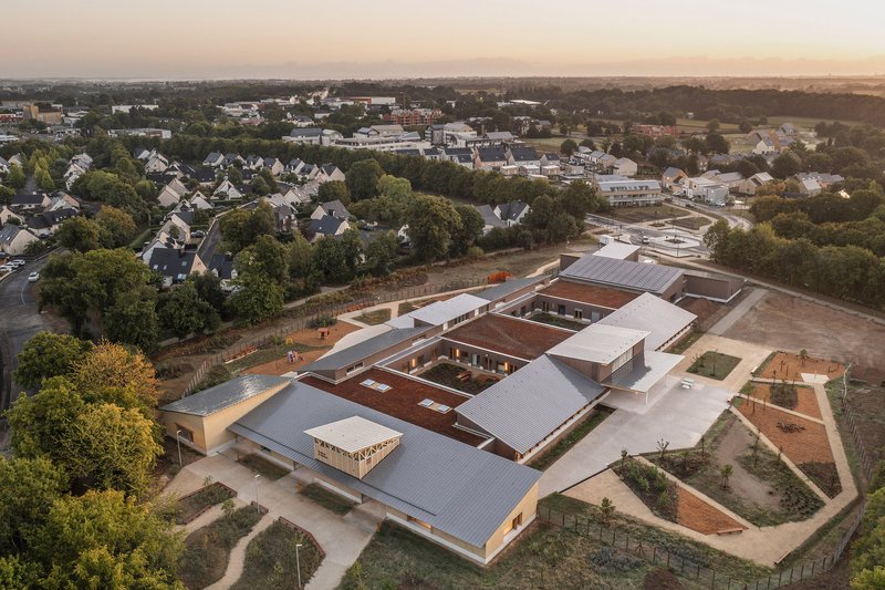 Aerial view at sunset of courtyard complex with metal roofs and planted beds surrounded by suburban neighborhood