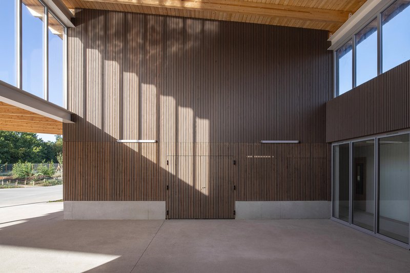 Covered porch with vertical timber slat walls and timber ceiling under angular sunlight shadows