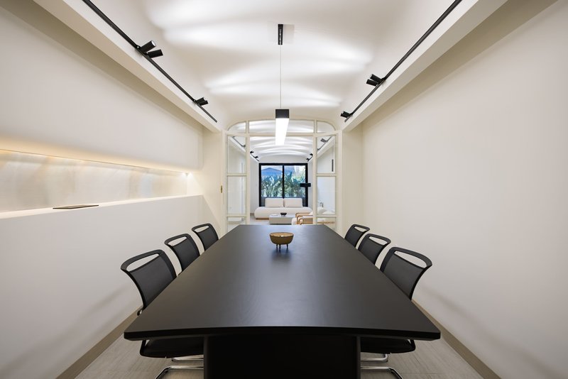 Conference room with dark table and mesh chairs beneath linear track lights and recessed cove lighting