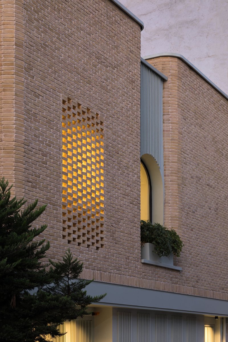 Curved brick facade with a perforated checkerboard screen and arched window with planter at dusk