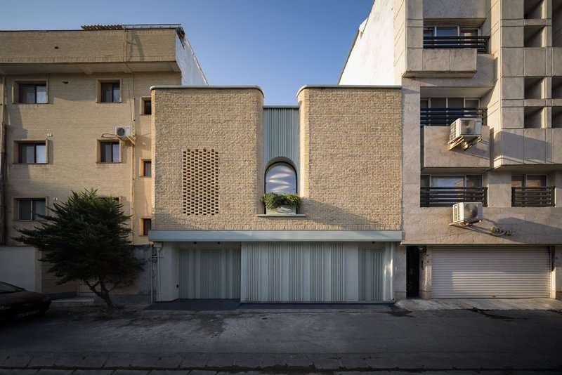 Street view of the buff brick facade with arched window and perforated screen between neighboring buildings