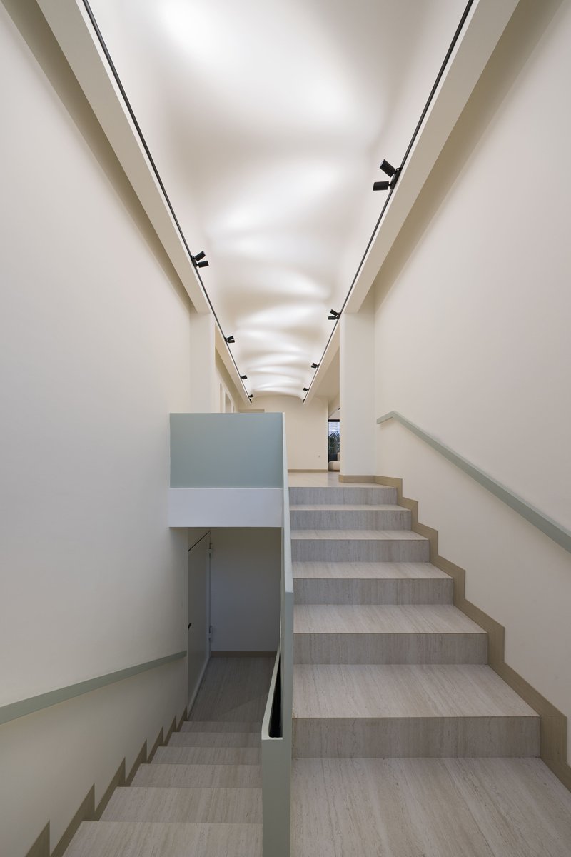 Interior stairwell with light wood treads and linear recessed lighting along the vaulted white ceiling