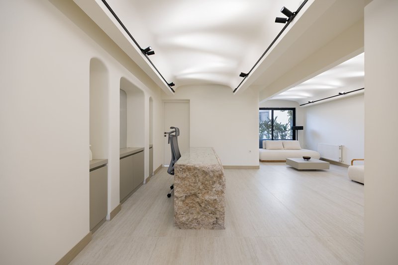 Open living space with arched doorways, rough stone bench and track lighting along the vaulted ceiling