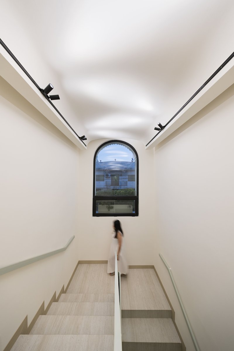 Interior stairwell with arched window at the landing and a figure descending the pale stone steps