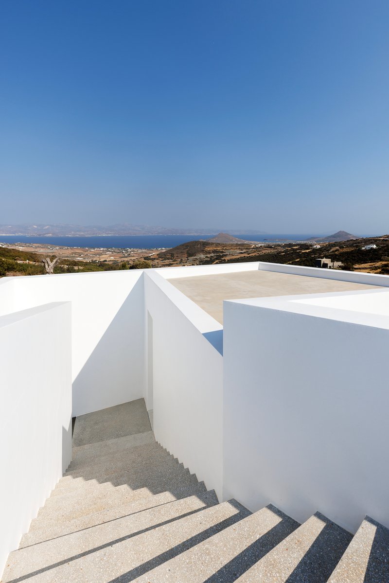 Terrazzo staircase descending between white rendered walls with a coastal landscape beyond