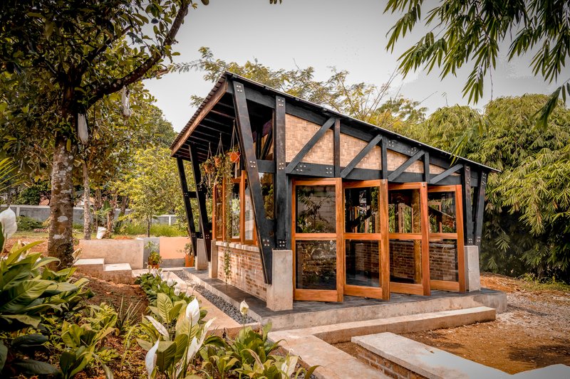 Angled view of the gabled facade with black steel frame and folding timber doors framed by garden planting